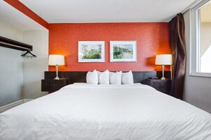 Hotelkamer met een groot bed, twee nachtkastjes met lampen, een rode accentmuur en twee ingelijste foto's.