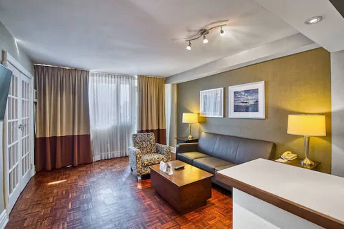 A hotel room with a wooden floor, a sofa, a chair, a coffee table, a desk, and two lamps.