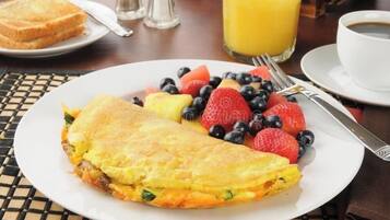 A breakfast plate with an omelette, strawberries, blueberries, and a glass of orange juice.