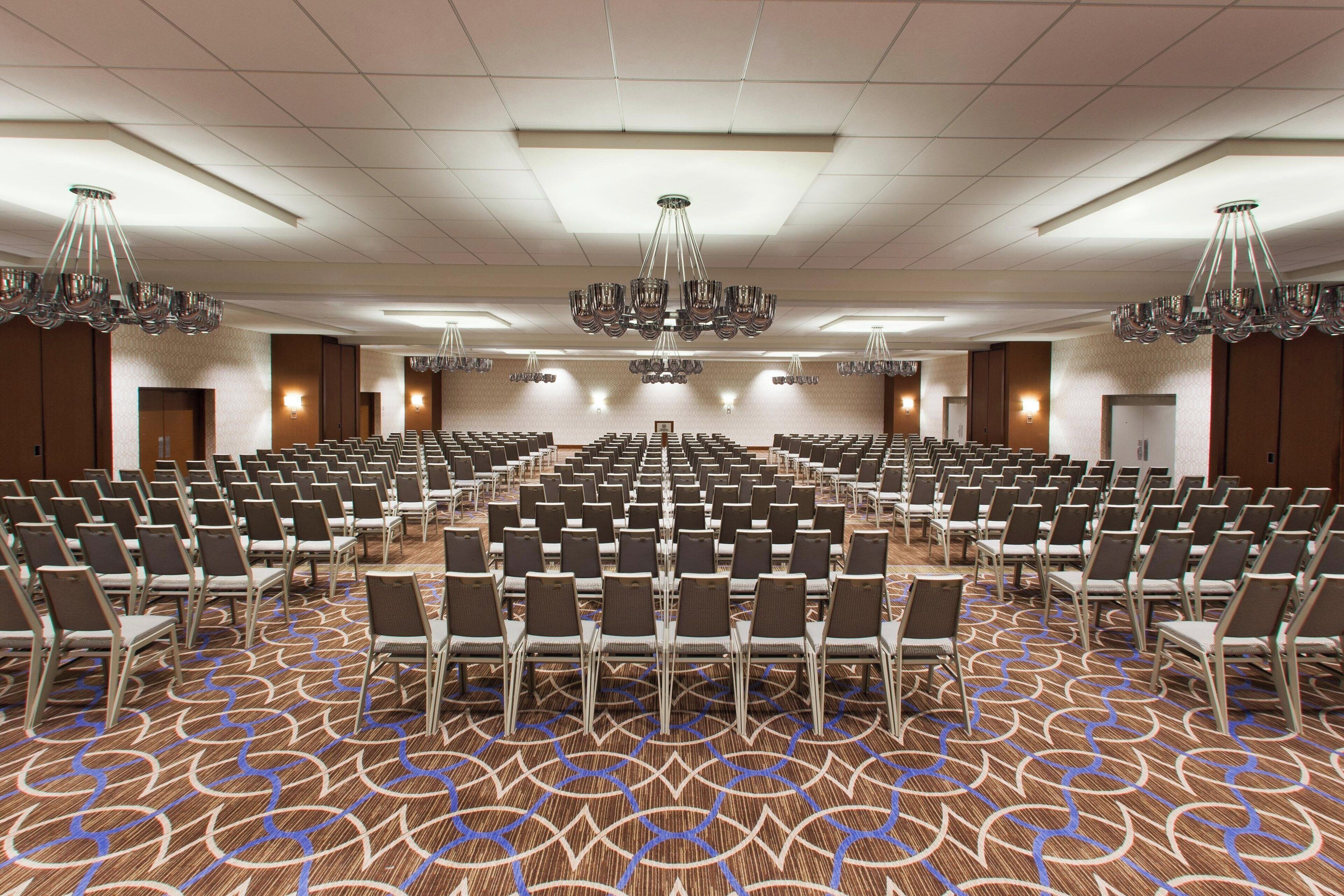 A large conference room with rows of chairs, a patterned carpet, and multiple chandeliers.