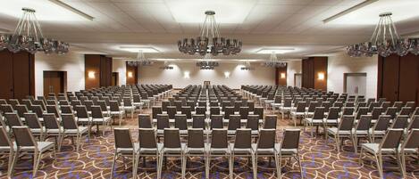 A large conference room with rows of chairs, a patterned carpet, and multiple chandeliers.