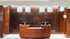 A reception desk with a wooden finish, two black chairs, and three wall-mounted lamps.