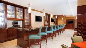 A bar area with a marble countertop, multiple bar stools, and a television mounted on the wall.