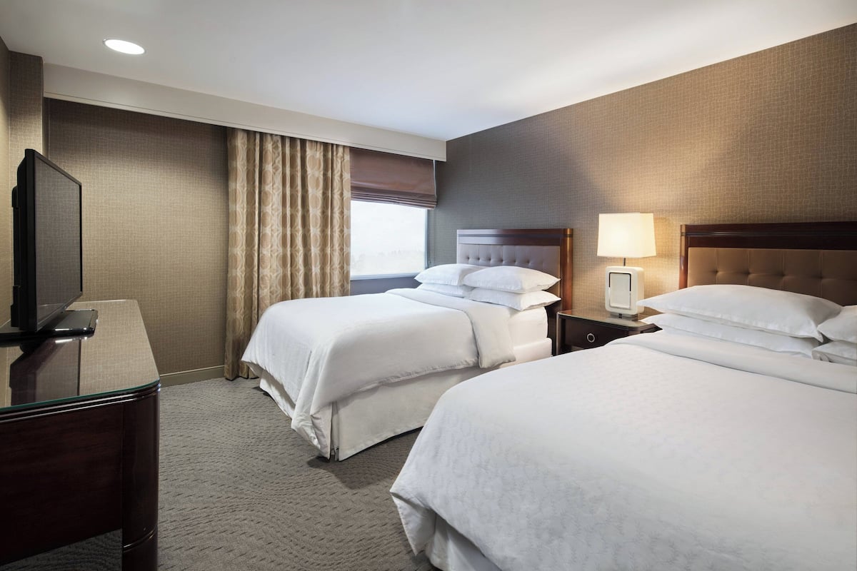 A hotel room with two beds, a TV, a desk, and a lamp.