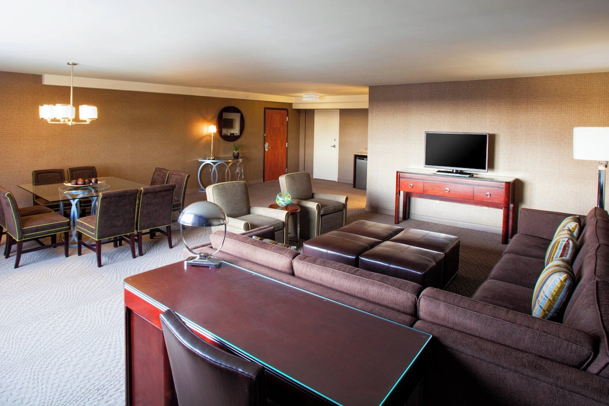 A hotel room with a dining area, a sofa set, a television, and a desk.