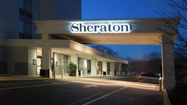 A Sheraton hotel entrance with a prominent sign, a parking lot, and a building facade.