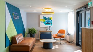 Un espace de détente moderne avec un canapé en cuir, une table basse ronde et un fauteuil orange. Un mur coloré orné d’un motif géométrique et une inscription qui dit : « Il suffit d’une étincelle. »