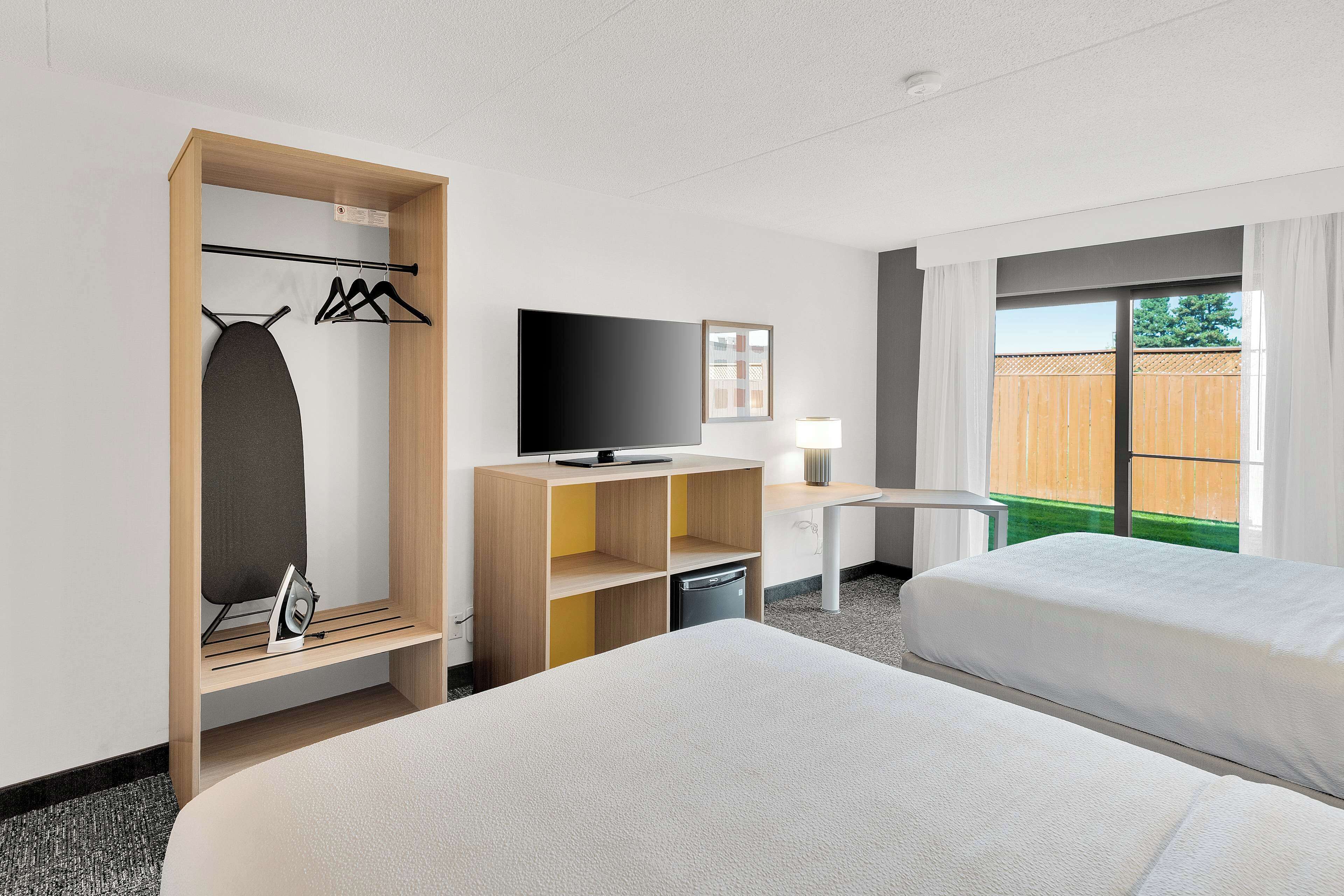 Een hotelkamer met twee bedden, een televisie, een bureau, een kledingkast en een raam met uitzicht op een hek.