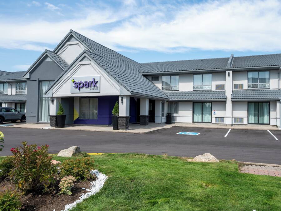 A hotel named 'Spark by Hilton' with a modern design, a parking lot, and a landscaped garden area.