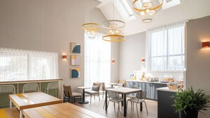 A modern dining area with wooden tables and chairs, pendant lighting, and a view of the kitchen area.