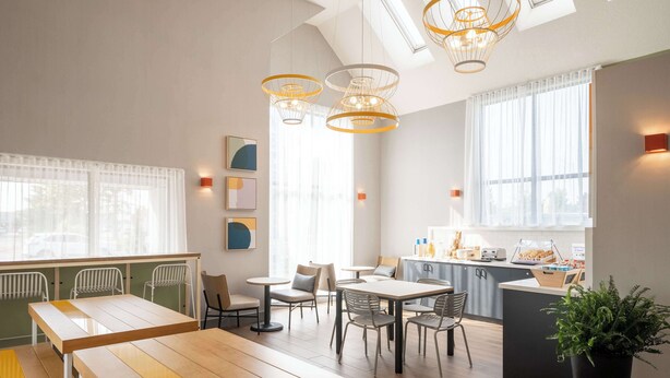 Un espace repas moderne avec des tables et des chaises en bois, des luminaires suspendus et une vue sur la cuisine.