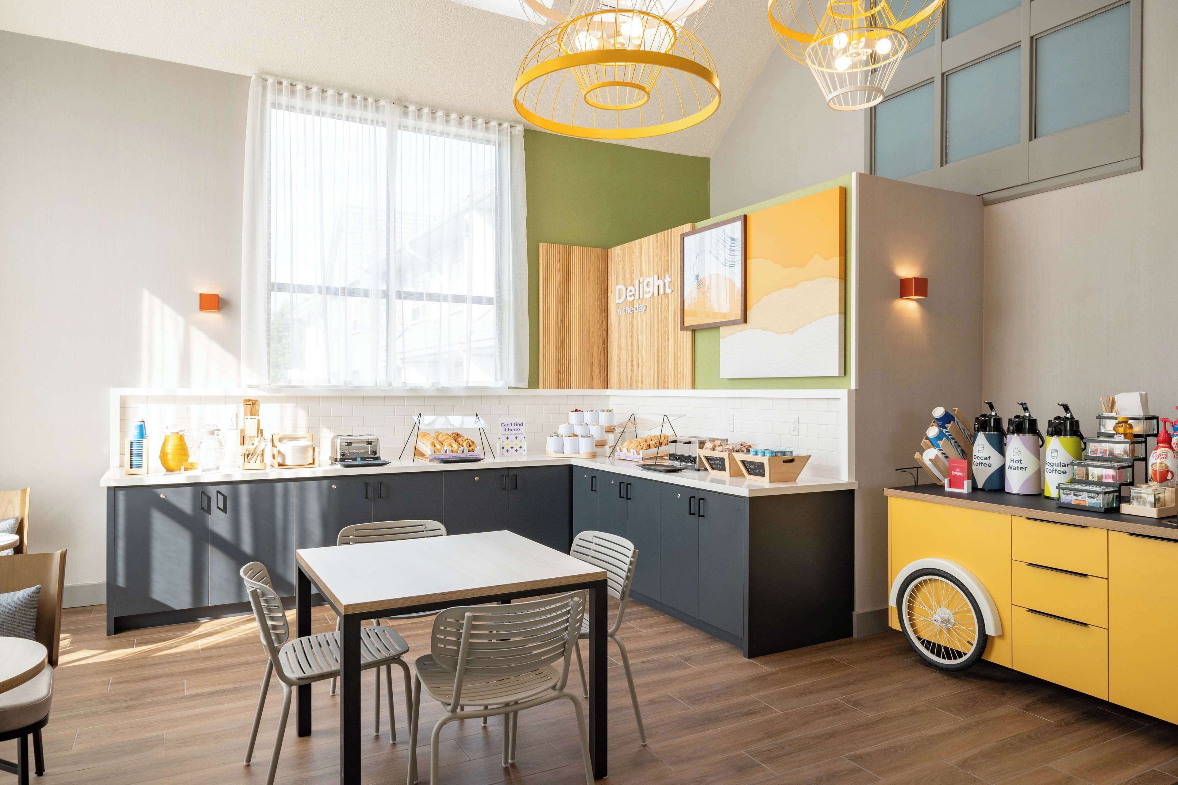 A modern kitchen with a dining area, featuring a large island, pendant lights, and a variety of kitchen appliances and utensils.