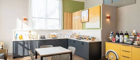 A modern kitchen with a dining area, featuring a large island, pendant lights, and a variety of kitchen appliances and utensils.