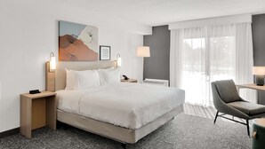 Une chambre d’hôtel avec un grand lit, un bureau, une chaise et une fenêtre avec des rideaux légers.