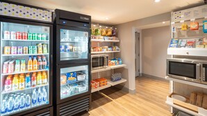 Un espace de libre-service où l’on peut se servir des boissons, avec des distributeurs réfrigérés et des étagères remplies de collations et d’eau en bouteille.
