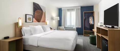 A hotel room with a large bed, bedside tables, a TV, a wardrobe, and a window with curtains.