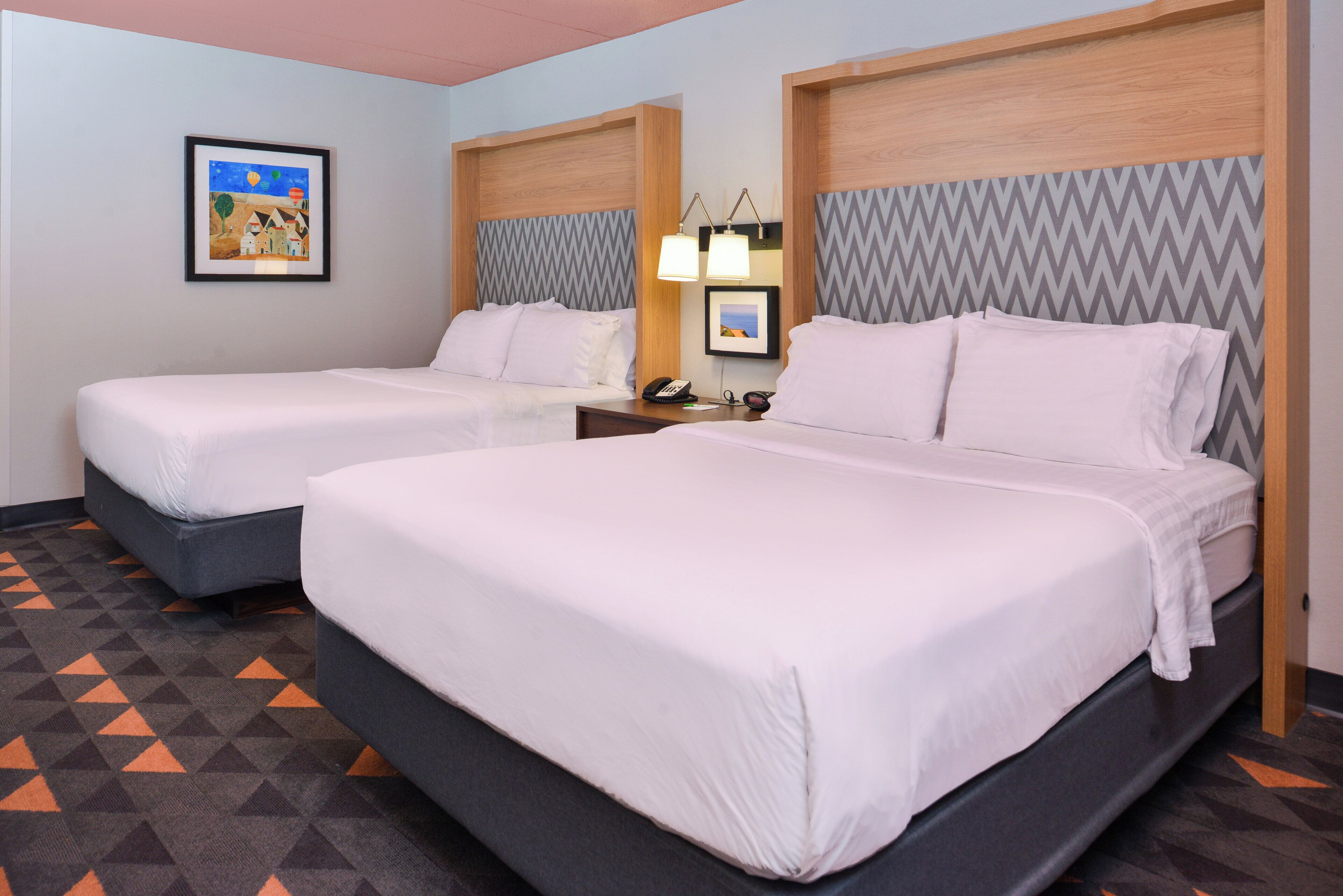A hotel room with two beds, a nightstand with a lamp, and a framed picture on the wall.