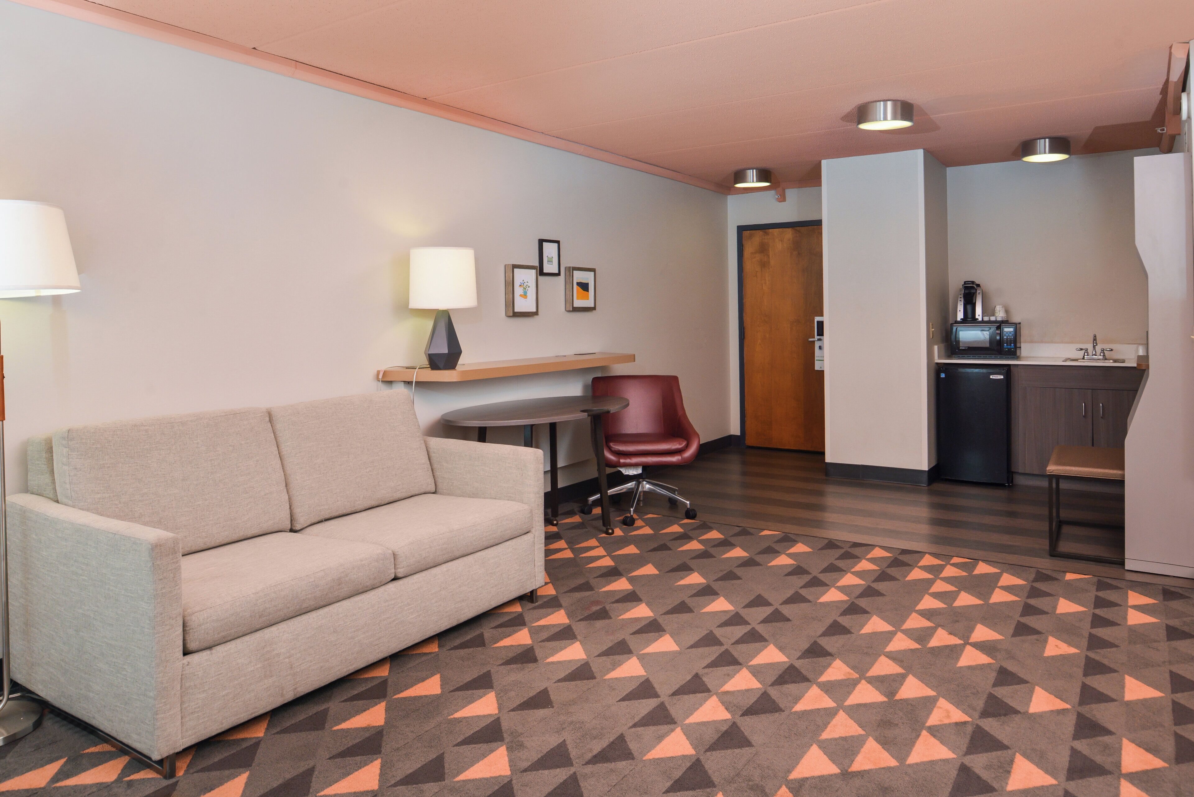 Ein Hotelzimmer mit einer Couch, einem kleinen Tisch, einem Sessel, einer Küchenzeile und einem gemusterten Boden.