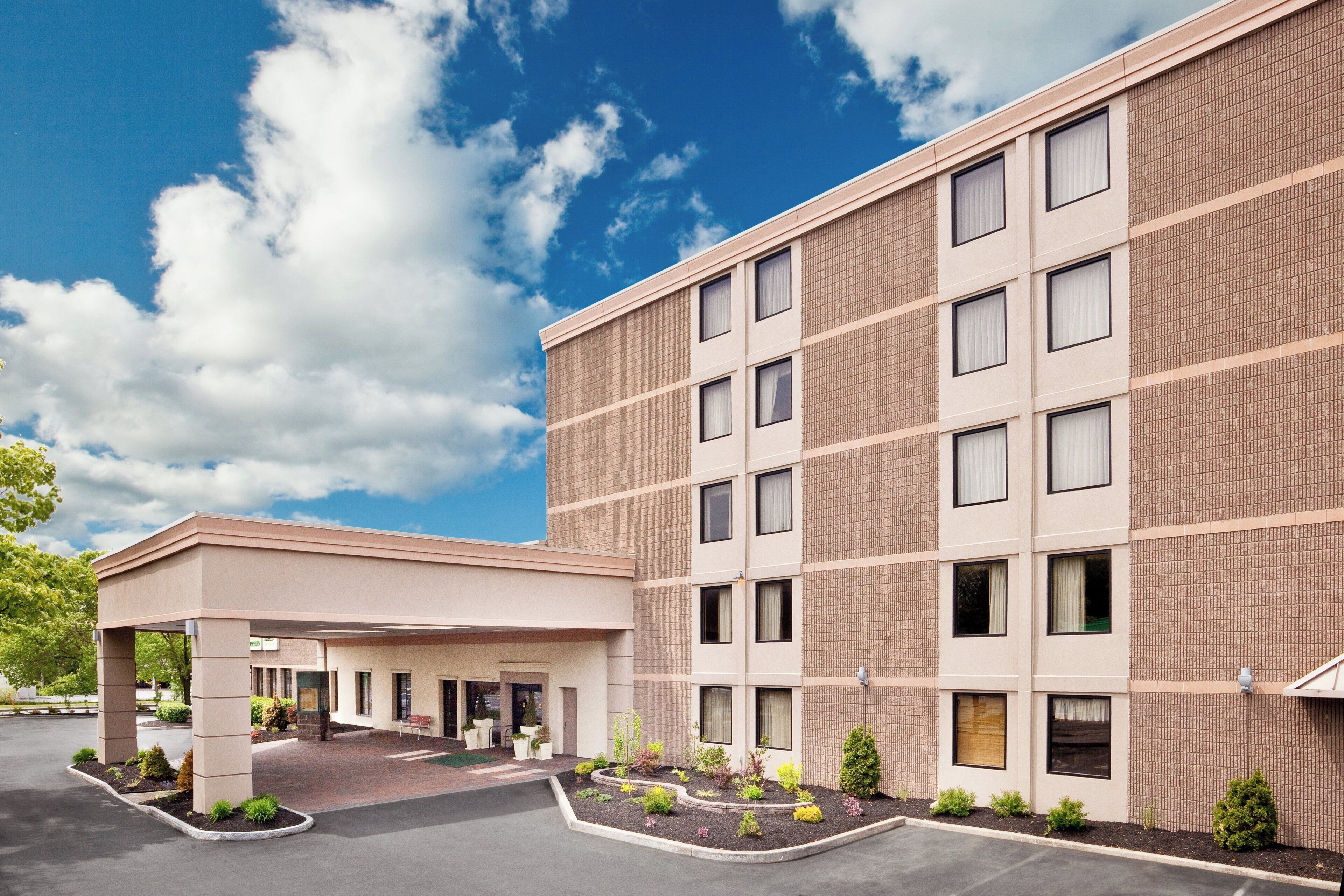 A multi-story hotel with a covered entrance and a landscaped garden area.