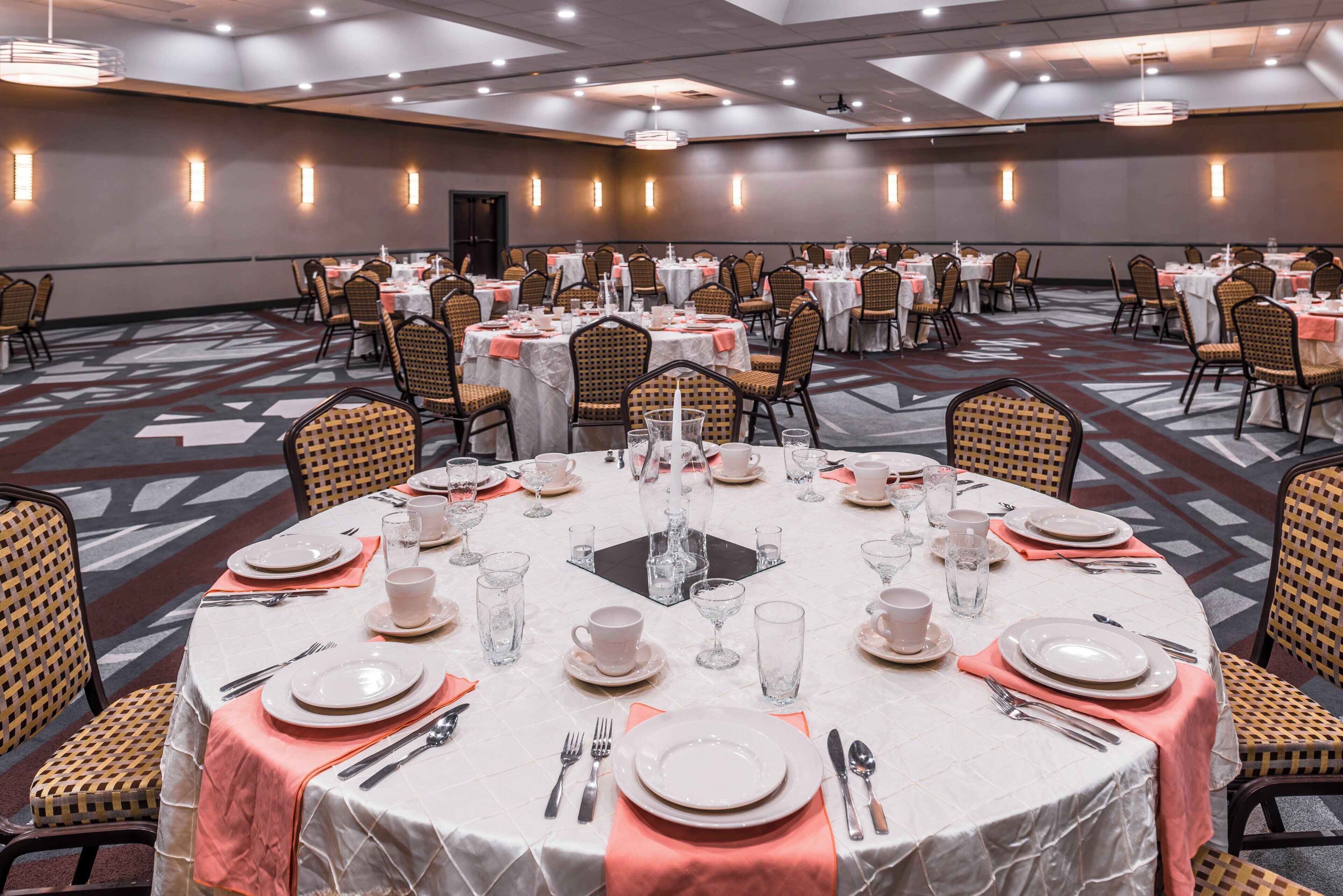 Un salón de banquetes con mesas redondas dispuestas para cenar, con platos, vasos y cubiertos.