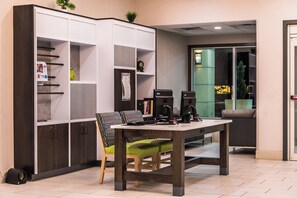 A modern office space with a large white shelving unit, a wooden table with a green chair, and two computer monitors. - Holiday Inn Auburn-Finger Lakes Region by IHG (Auburn)