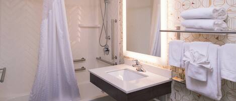 Un baño con bañera, ducha, lavabo con espejo y toallero con toallas dobladas.