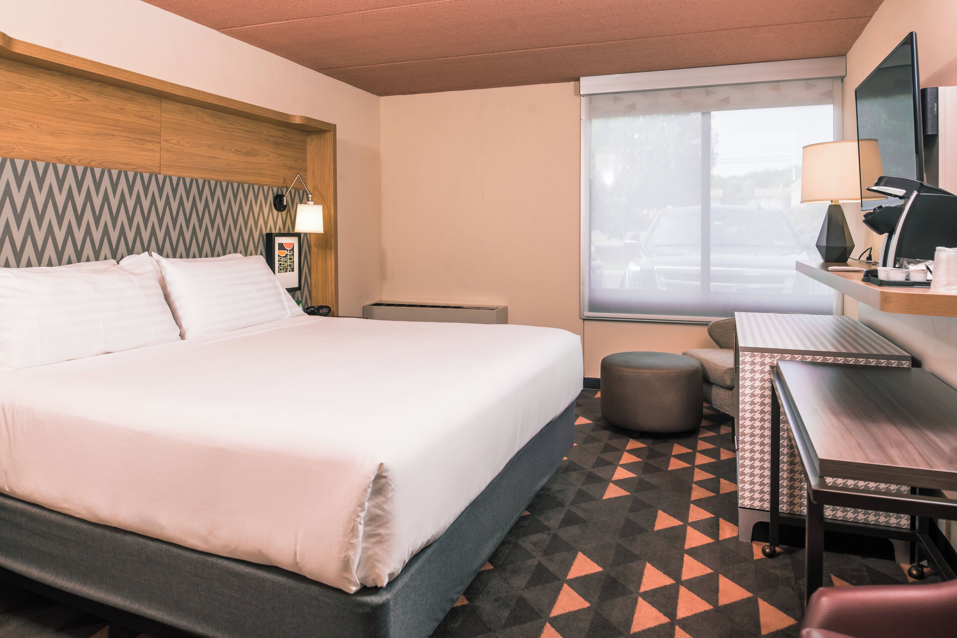 A hotel room with a bed, desk, chair, and a window with a view.