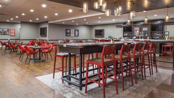 A restaurant with a long counter, red chairs, and hanging pendant lights.