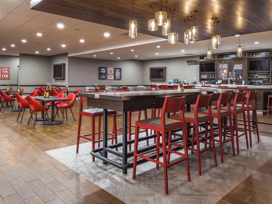 A restaurant with a long counter, red chairs, and hanging pendant lights.