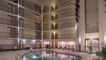 Interior de un hotel de varios pisos con un área de piscina central, múltiples balcones y un elevador para piscina.