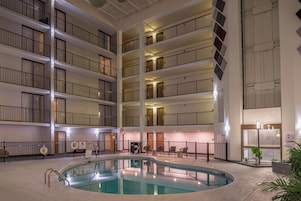 Interior de um hotel com vários andares, área de piscina central, diversas varandas e elevador para piscina.