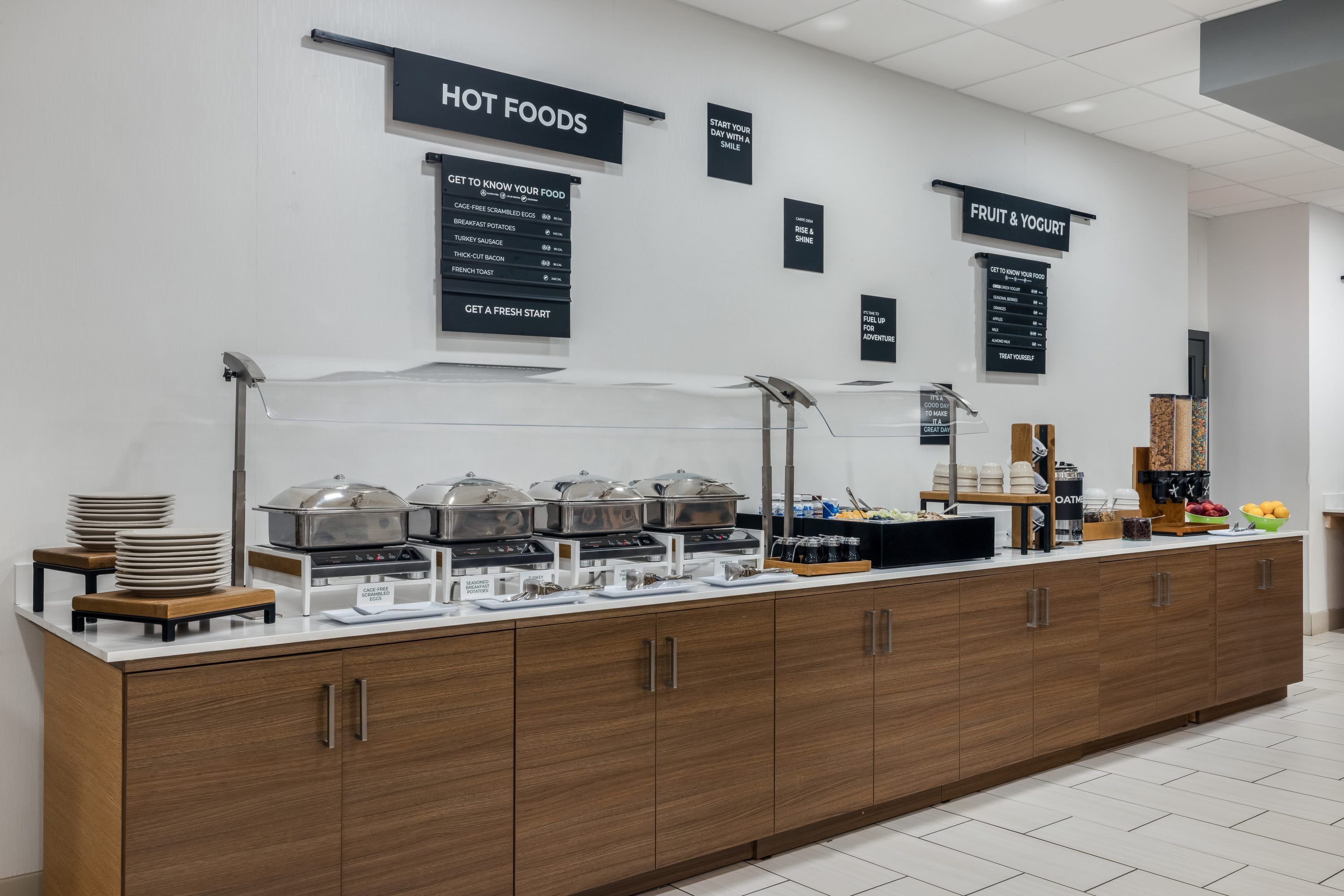A buffet setup with hot foods, fruit & yogurt, and a sign indicating a fresh start.