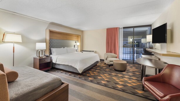 Une chambre d’hôtel avec un lit, un bureau, une chaise, une télévision et une fenêtre avec des rideaux.