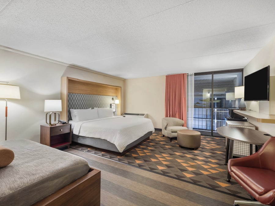 Ein Hotelzimmer mit Bett, Schreibtisch, Stuhl, Fernseher und einem Fenster mit Vorhängen.