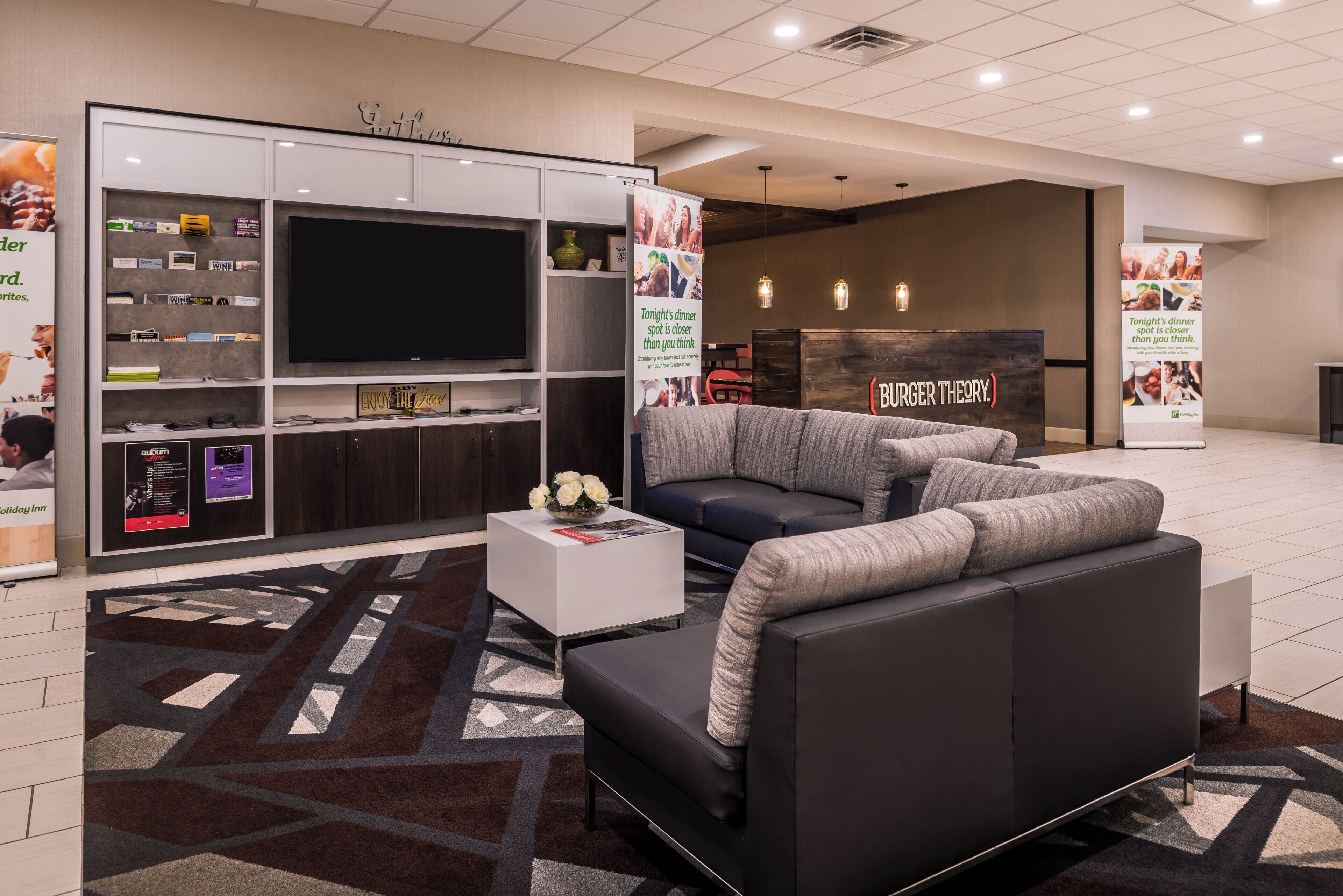 Eine moderne Hotellobby mit einem großen Flachbildfernseher, einer Couch, einem Couchtisch und einem gemusterten Teppich.