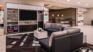 A modern hotel lobby with a large flat-screen TV, a sofa, a coffee table, and a patterned rug.