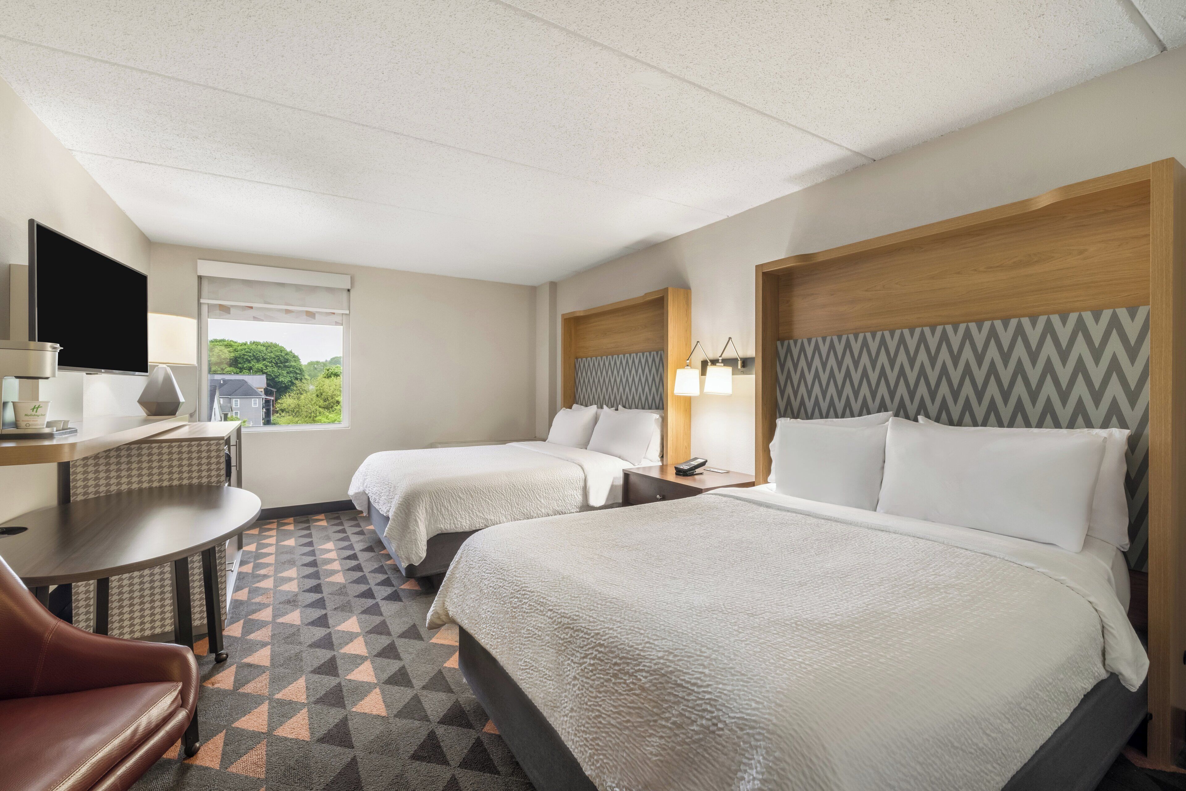 Une chambre d’hôtel avec deux lits, un bureau, une télévision et une vue sur la verdure environnante.