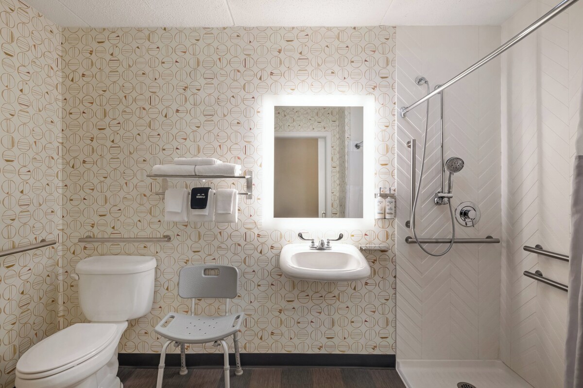 Un bagno con toilette, lavandino, specchio, doccia e una sedia.