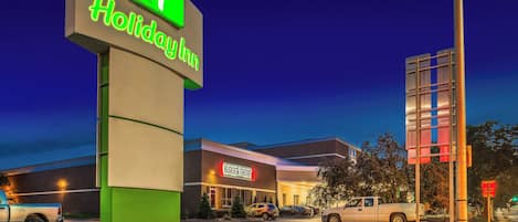 A Holiday Inn sign with a green and white logo, a brick building with a Burger Theory restaurant, and a parking lot with vehicles.
