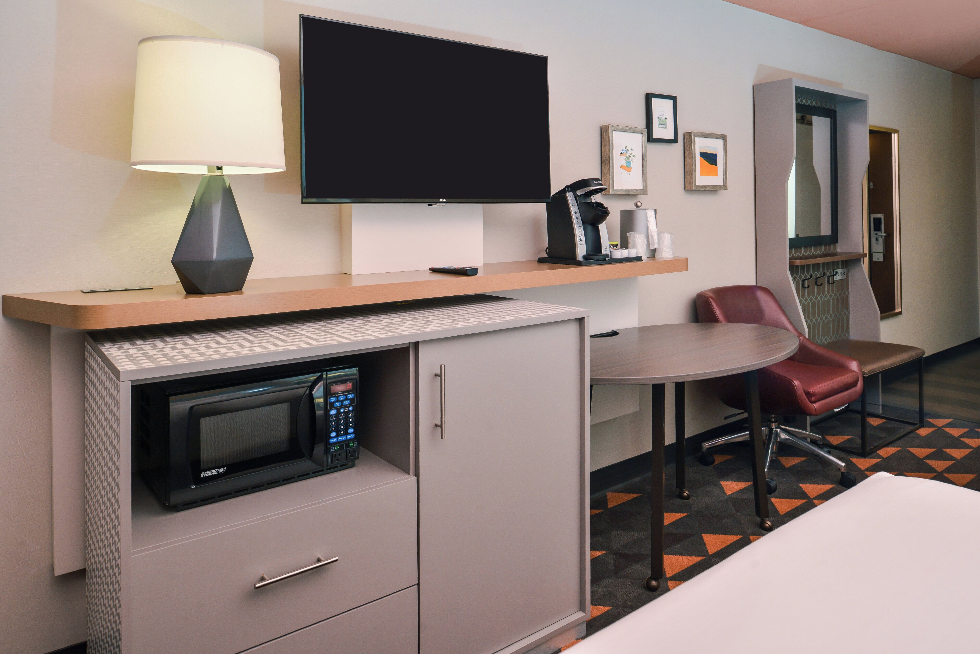 A hotel room with a flat-screen TV, a microwave, a coffee maker, a desk, a chair, and a bed.