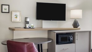 Une chambre d’hôtel équipée d’un téléviseur à écran plat, d’une lampe, d’un four à micro-ondes, d’une machine à café et d’un tableau encadré au mur.