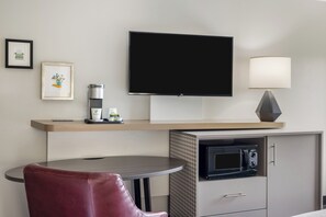 Una camera d'albergo con TV a schermo piatto, una lampada, un forno a microonde, una macchina per il caffè e un quadro appeso al muro.