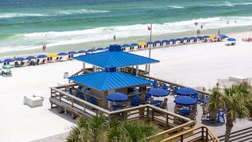 A beachside restaurant with outdoor seating and a blue roof, overlooking the ocean.