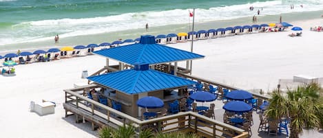 A beachside restaurant with outdoor seating and a blue roof, overlooking the ocean.