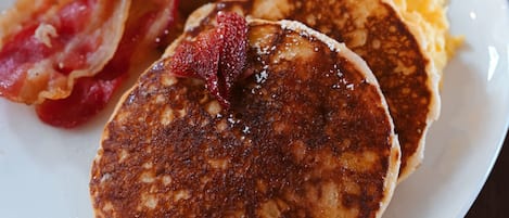 A breakfast plate with pancakes, bacon, eggs, and potatoes.