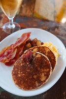 Un plato de desayuno con tortitas, tocino, huevos y papas.