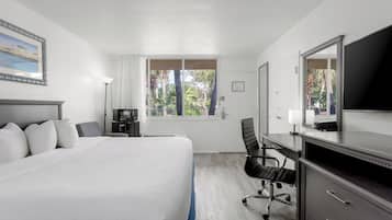 A hotel room with a large bed, a desk, a chair, a television, and a window with a view of trees.