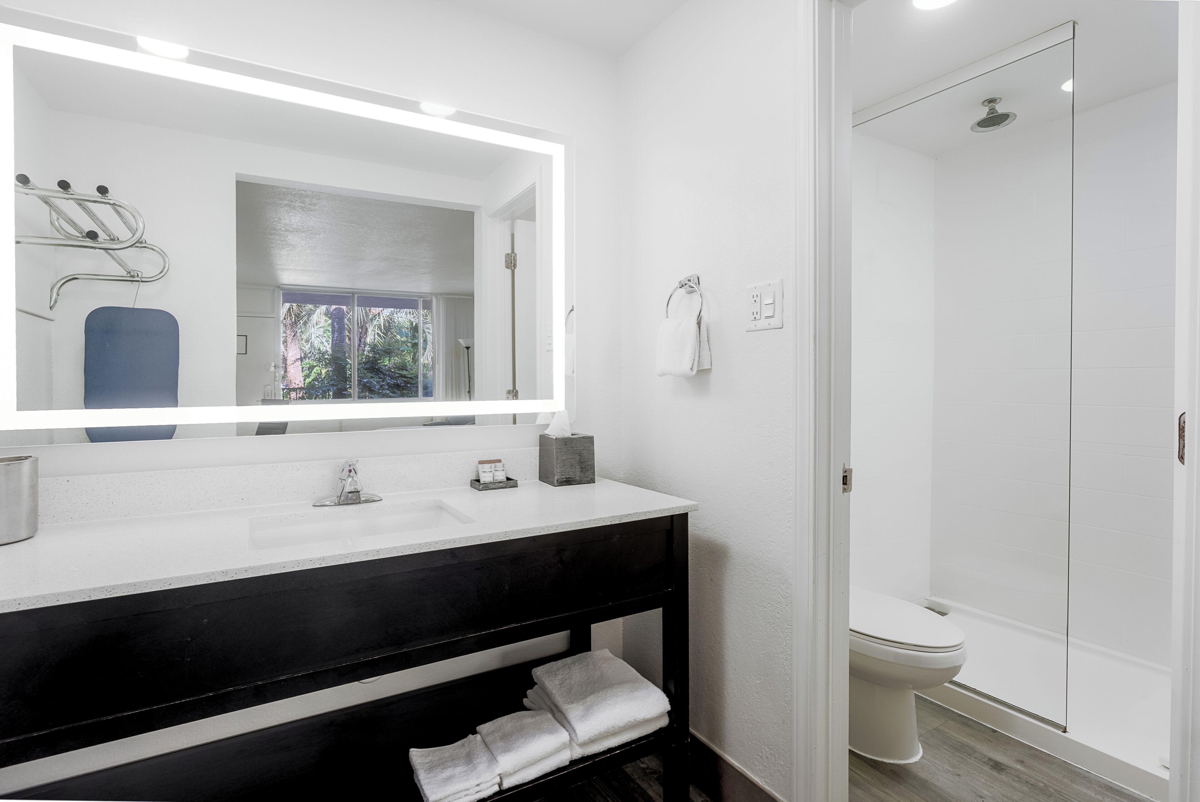 A modern bathroom with a white vanity, a large mirror, a shower, and a toilet.