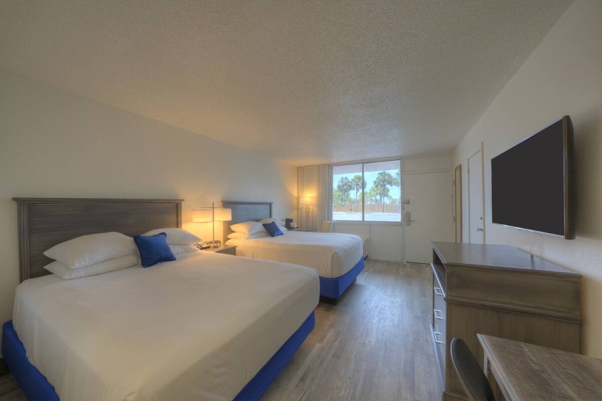 A hotel room with two beds, a desk, and a TV.