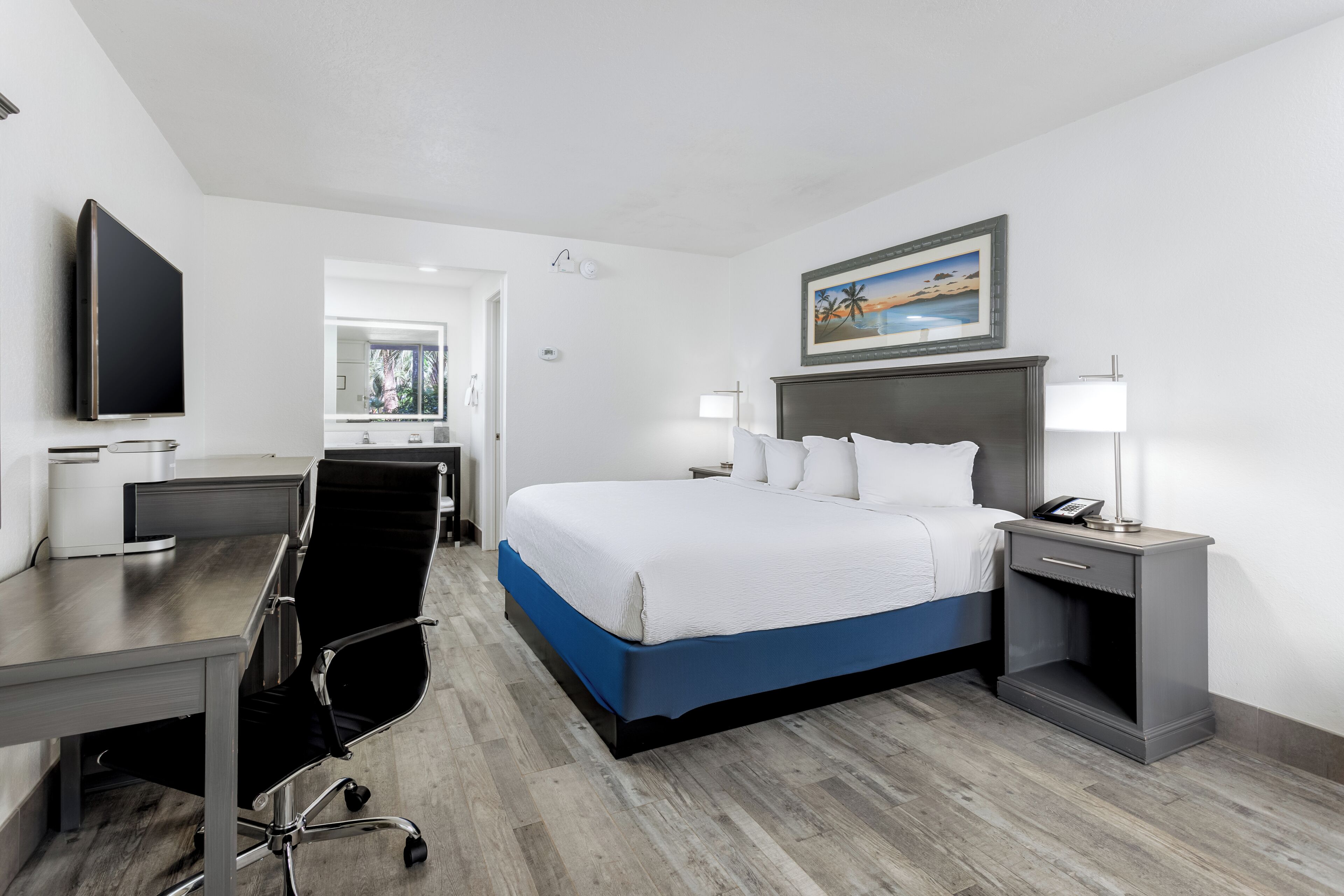 A hotel room with a bed, desk, chair, and a TV.